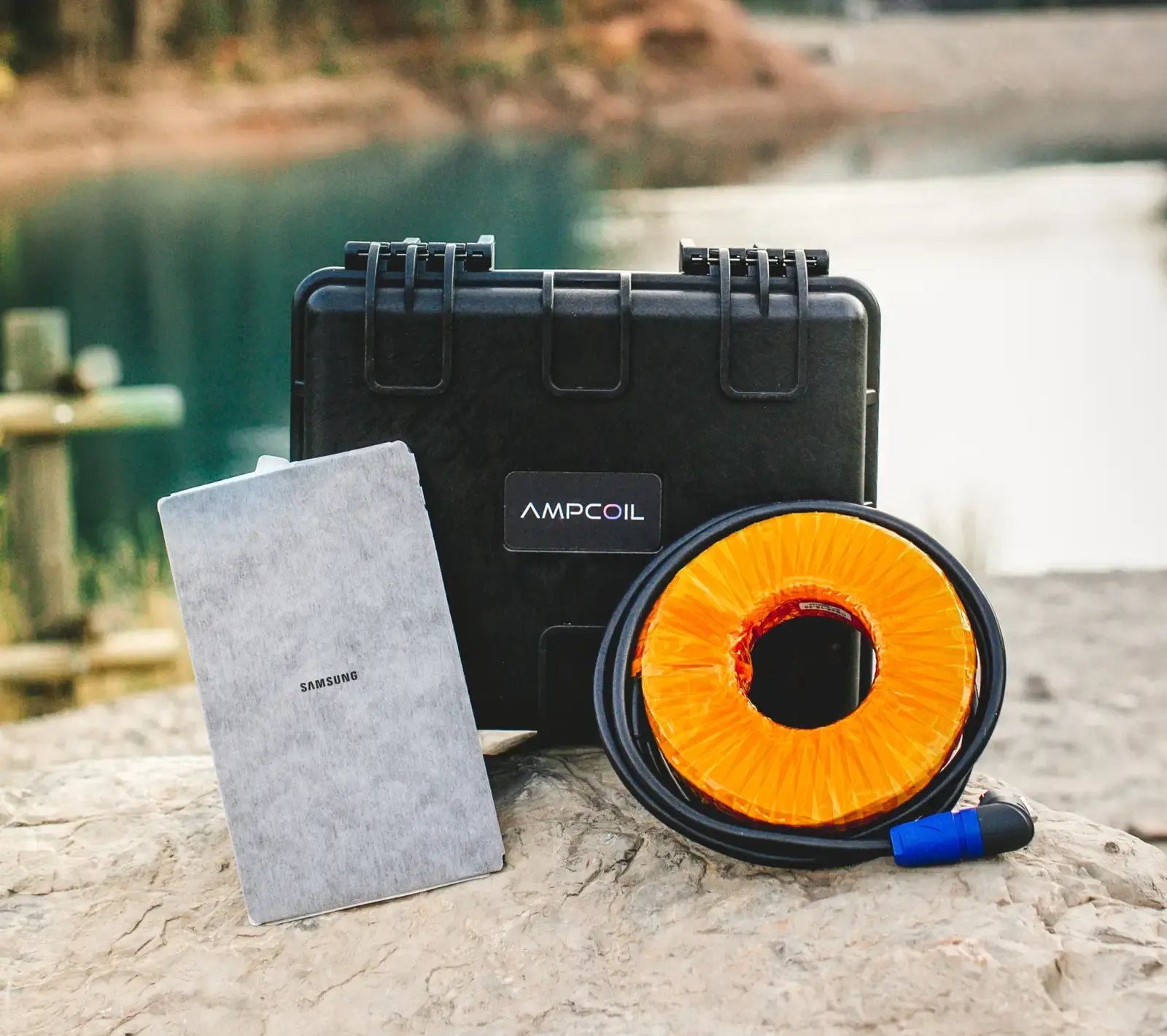 AmpCoil case, coil and tablet on a rock by a lake