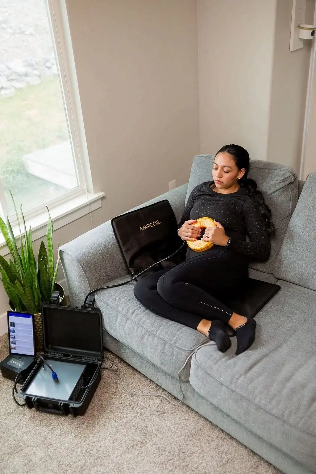 Woman relaxing on a sofa with the AmpCoil coil and PEMF Mat