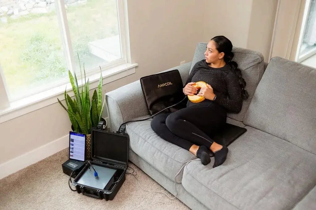 Woman relaxing on a sofa with the AmpCoil coil and PEMF Mat