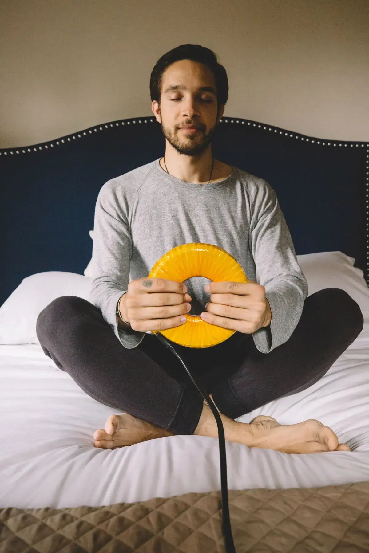Man sitting cross-legged on a bed holding the AmpCoil coil